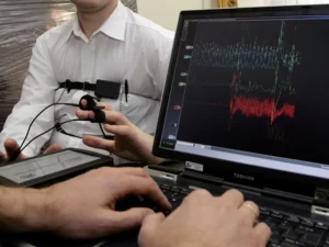An examinee is attached to the polygraph machine while the examiner observes the results.