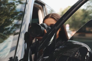 A female investigator takes a photograph behind a parked car.